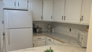 A kitchen with white cabinets, a marble countertop, a refrigerator, a toaster, and a coffee maker. - Enjoy Beautiful Sunsets on Lake Reno (Alexandria)