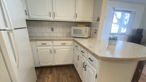 A modern kitchen with white cabinetry, a wooden floor, a microwave, and a window with natural light. - Enjoy Beautiful Sunsets on Lake Reno (Alexandria)