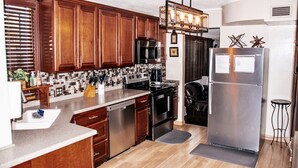 A modern kitchen with wooden cabinets, stainless steel appliances, and a black countertop. - Upscale Abode  (Wichita)