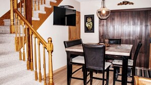 A dining area with a wooden staircase, a flat-screen TV mounted on the wall, and a chandelier. - Upscale Abode  (Wichita)