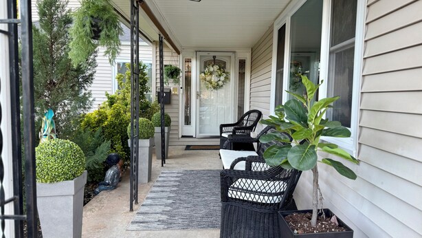 A covered porch with outdoor furniture, potted plants, and a door with a wreath. - Upscale Abode  (Wichita)