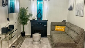 A living room with a sofa, a coffee table, a fireplace, a television, and a potted plant. - Upscale Abode  (Wichita)