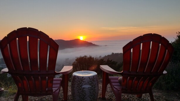 Two Adirondack chairs facing a sunset over a mountainous landscape with a table between them. - Cozy, modern 1-bedroom guest suite with backyard ocean view! (Pacifica)