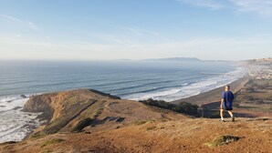 A person standing on a cliff overlooking a coastal landscape with a view of the ocean and distant hills. - Cozy, modern 1-bedroom guest suite with backyard ocean view! (Pacifica)