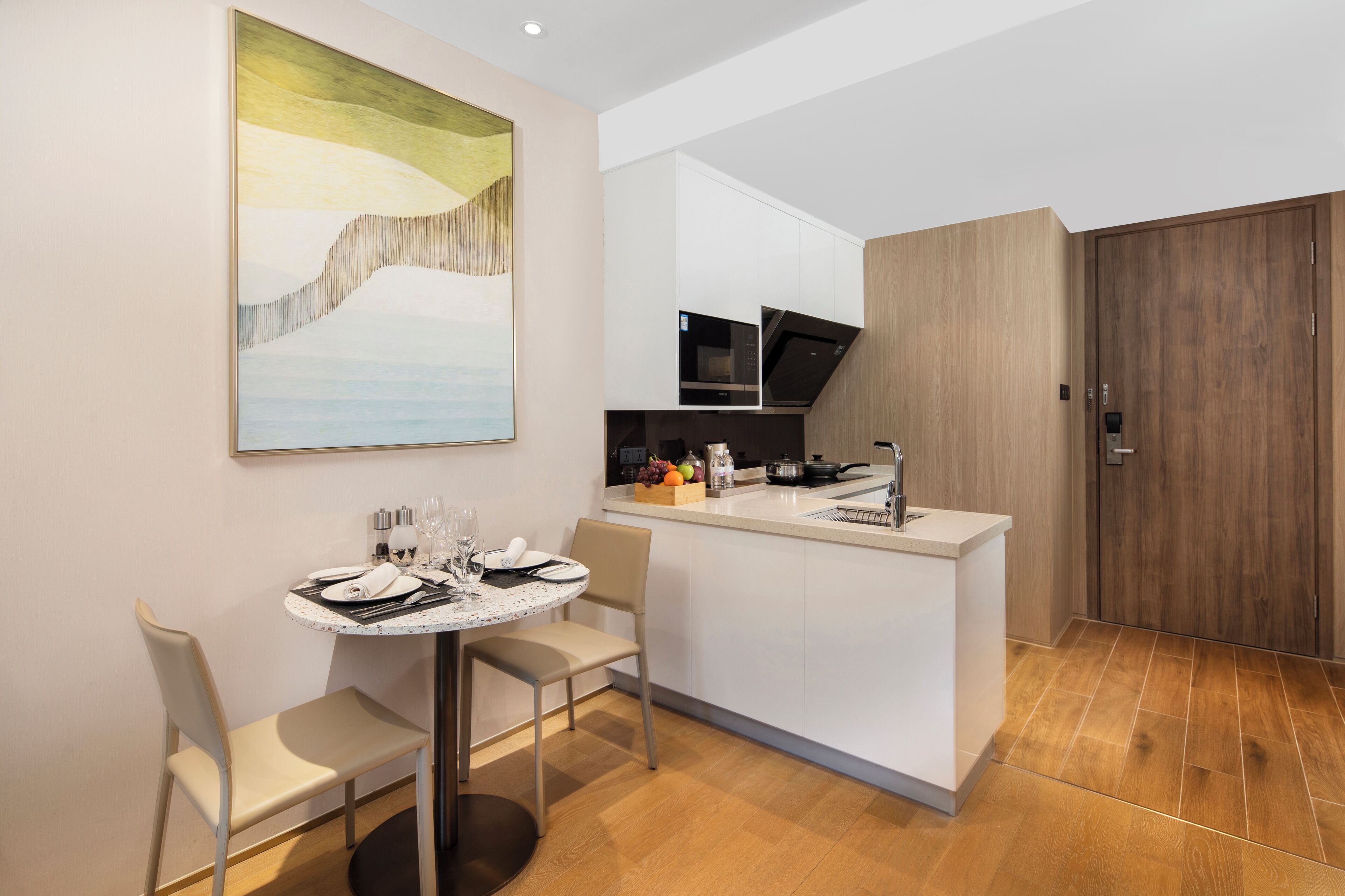 A modern kitchen with a central island, a dining area with a round table, and a large abstract painting on the wall.