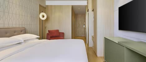A modern hotel room with a large bed, a red chair, a TV mounted on the wall, and a wooden door.