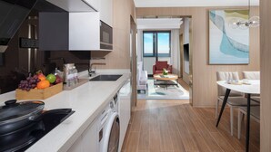 A modern kitchen with a built-in oven, a washing machine, and a fruit bowl. There is a dining area with a table and chairs, and a view of the sea through a large window. - Hyatt Place Shanghai Lingang (Shanghai)