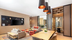 A modern living room with a sofa, coffee table, and dining table. There are shelves with decorative items and a TV mounted on the wall. - Hyatt Place Shanghai Lingang (Shanghai)