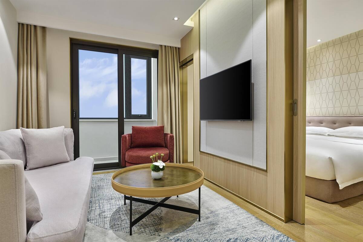 A hotel room with a sofa, armchair, round coffee table, and a bed.