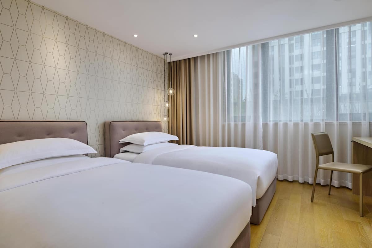 A hotel room with two beds, a desk, a chair, and a large window with curtains.