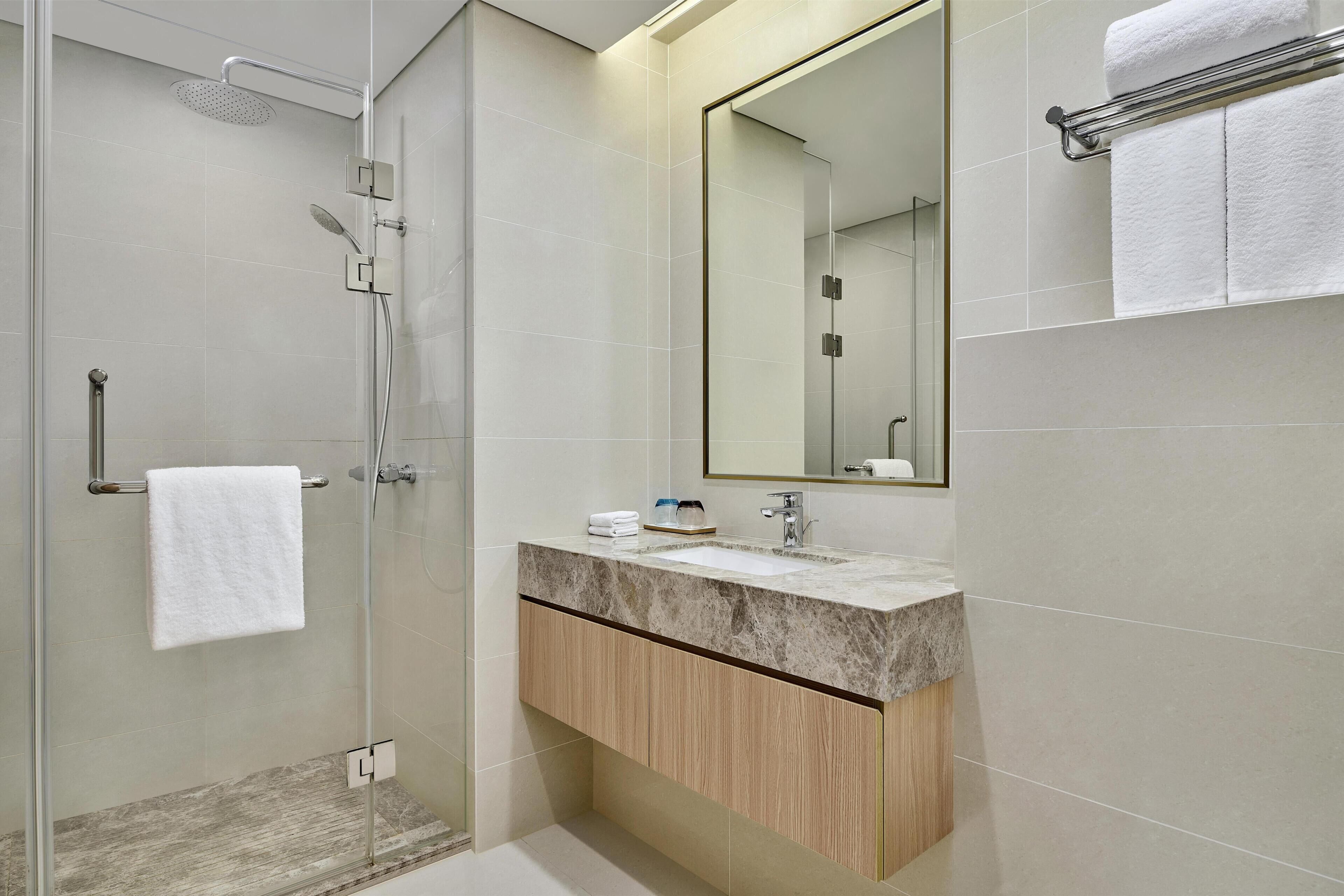 A modern bathroom with a glass shower enclosure, a marble sink, and a wooden vanity.