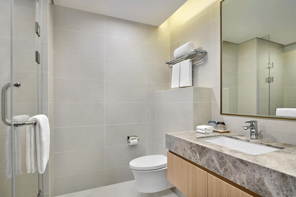 A modern bathroom with a glass shower enclosure, a toilet, a sink with a marble countertop, and a mirror.