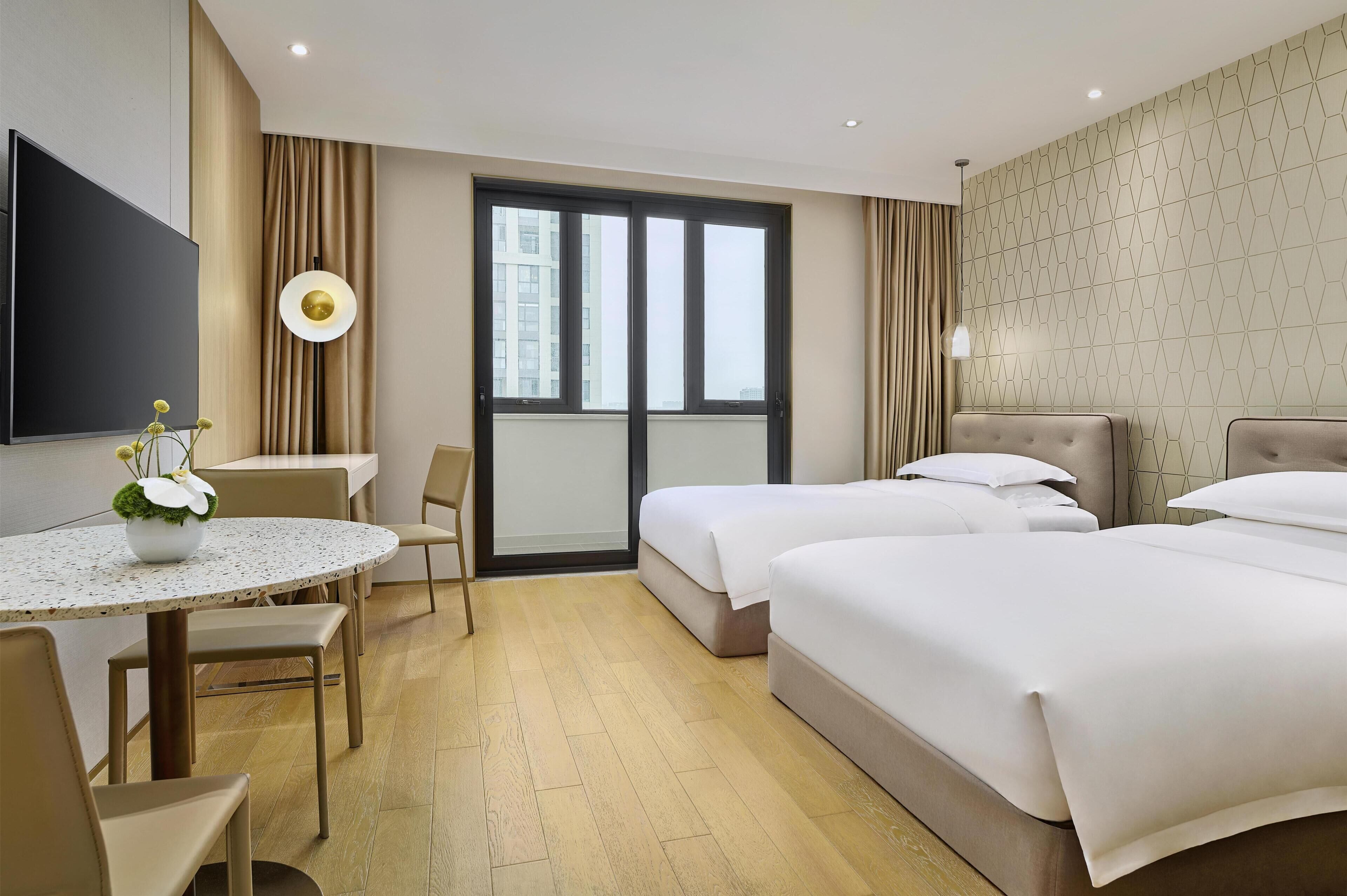 A hotel room with a bed, a desk, a chair, a TV, and a window.