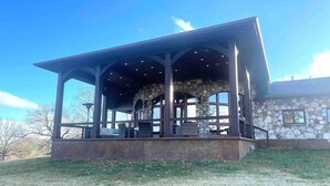 A covered outdoor area with stone walls and a roof, featuring seating and a stone fireplace. - LAKEFRONT ON GRAND LAKE “THE LODGE” AT STONY POINT (Jay)