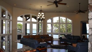 A spacious living area with a large glass table, multiple seating arrangements, and a view of the outdoors. - LAKEFRONT ON GRAND LAKE “THE LODGE” AT STONY POINT (Jay)
