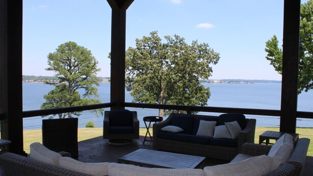A covered outdoor seating area with wicker furniture, a view of a lake, and a gazebo structure. - LAKEFRONT ON GRAND LAKE “THE LODGE” AT STONY POINT (Jay)