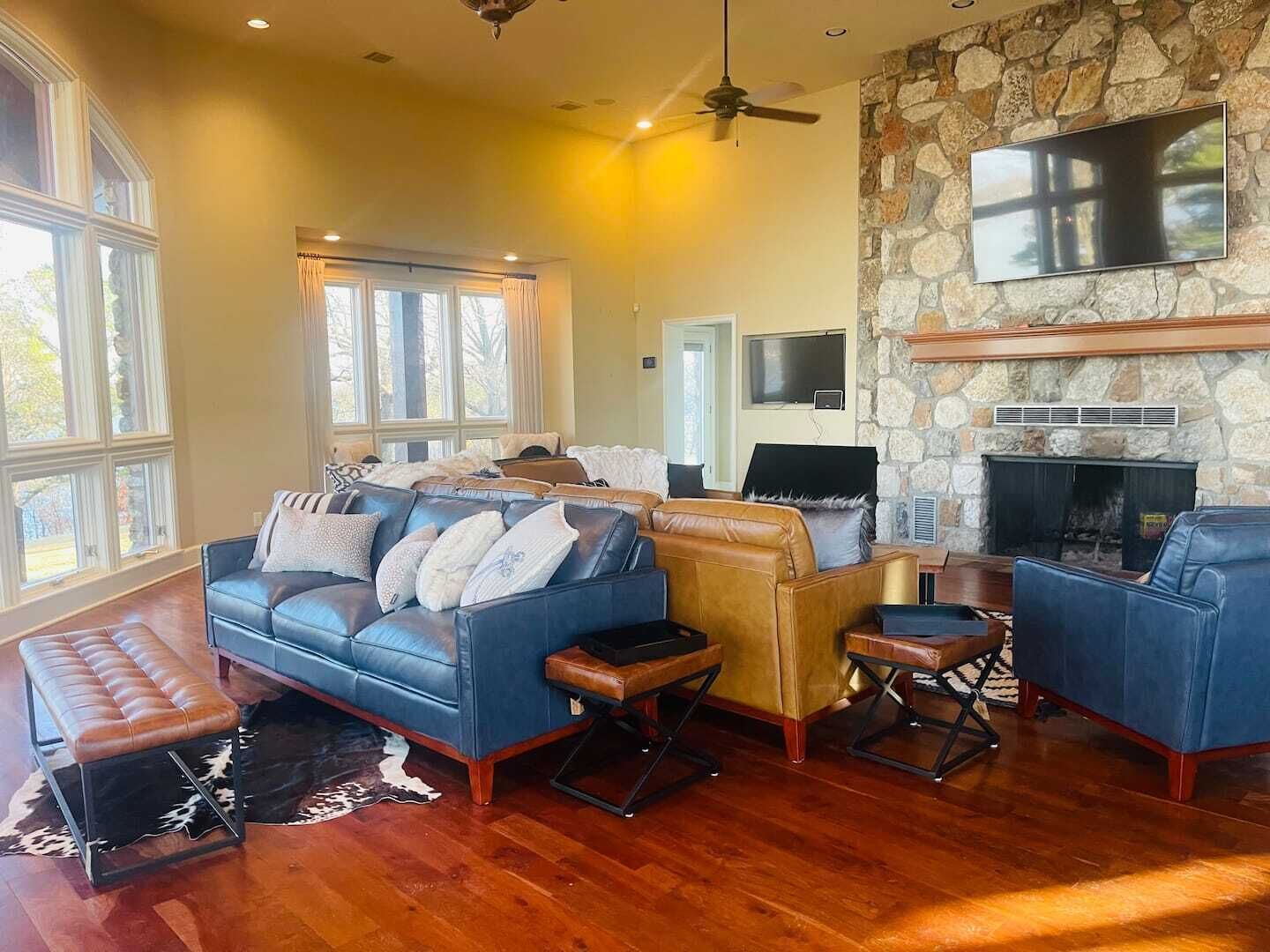 A spacious living room with a stone fireplace, leather sofas, and a large TV mounted on the wall.