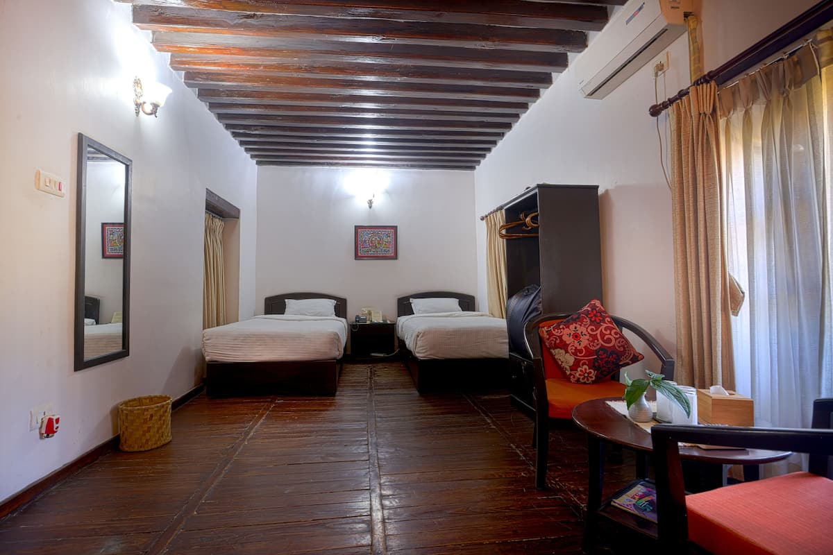 A room with two beds, a wooden ceiling, a mirror, a small table with a plant, and a chair.