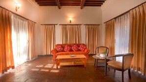 A living room with a sofa, a coffee table, and a chair. There are curtains on the windows and a ceiling light. - Hukum Darbar Restaurant & Hotel (Kathmandu)