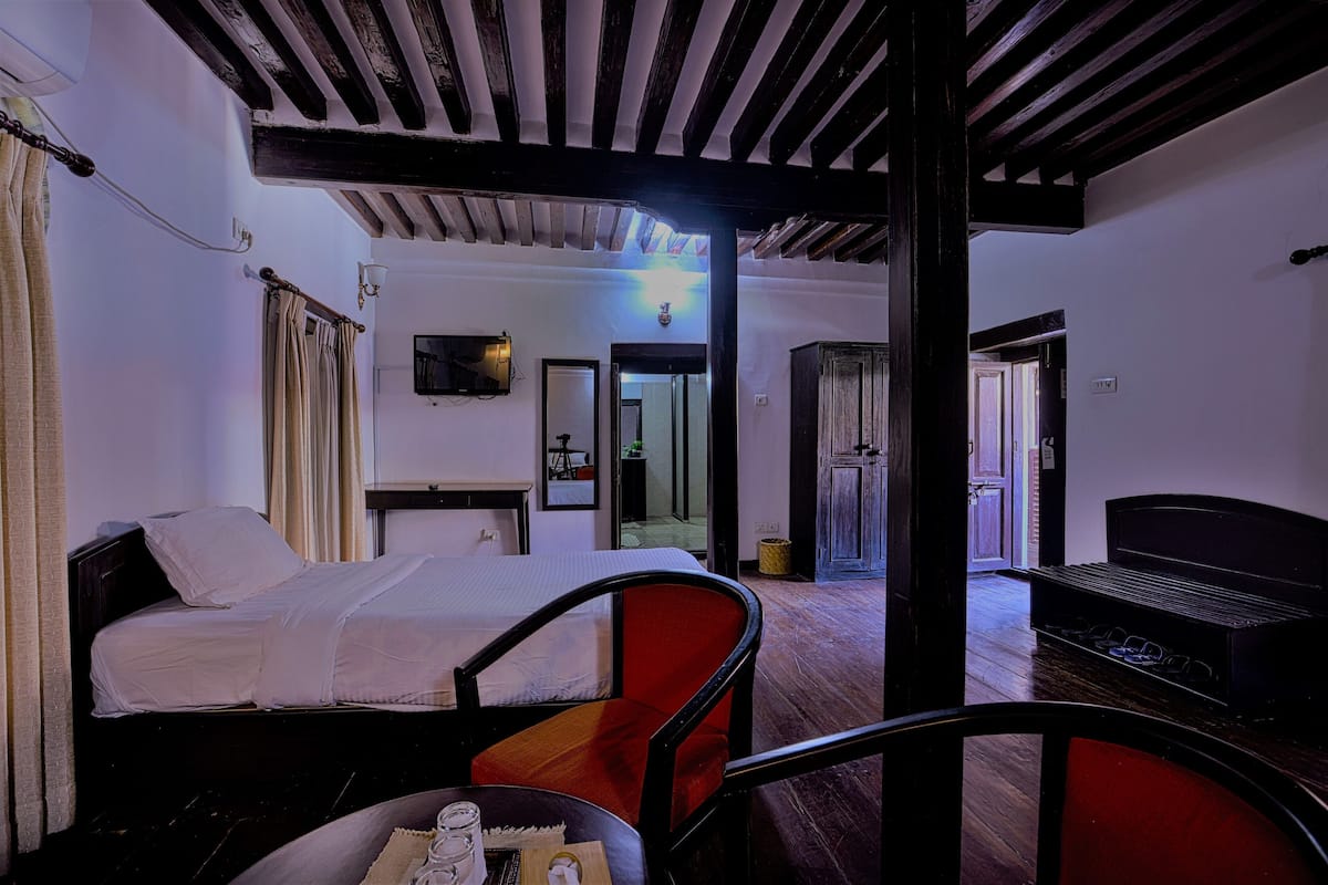 A hotel room with a bed, a chair, a table with a glass, and a bench.