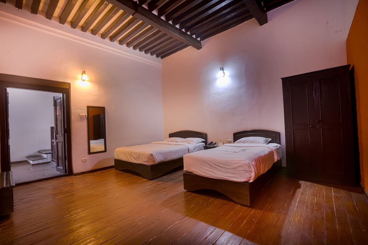 A room with two beds, wooden flooring, a wardrobe, and a mirror.
