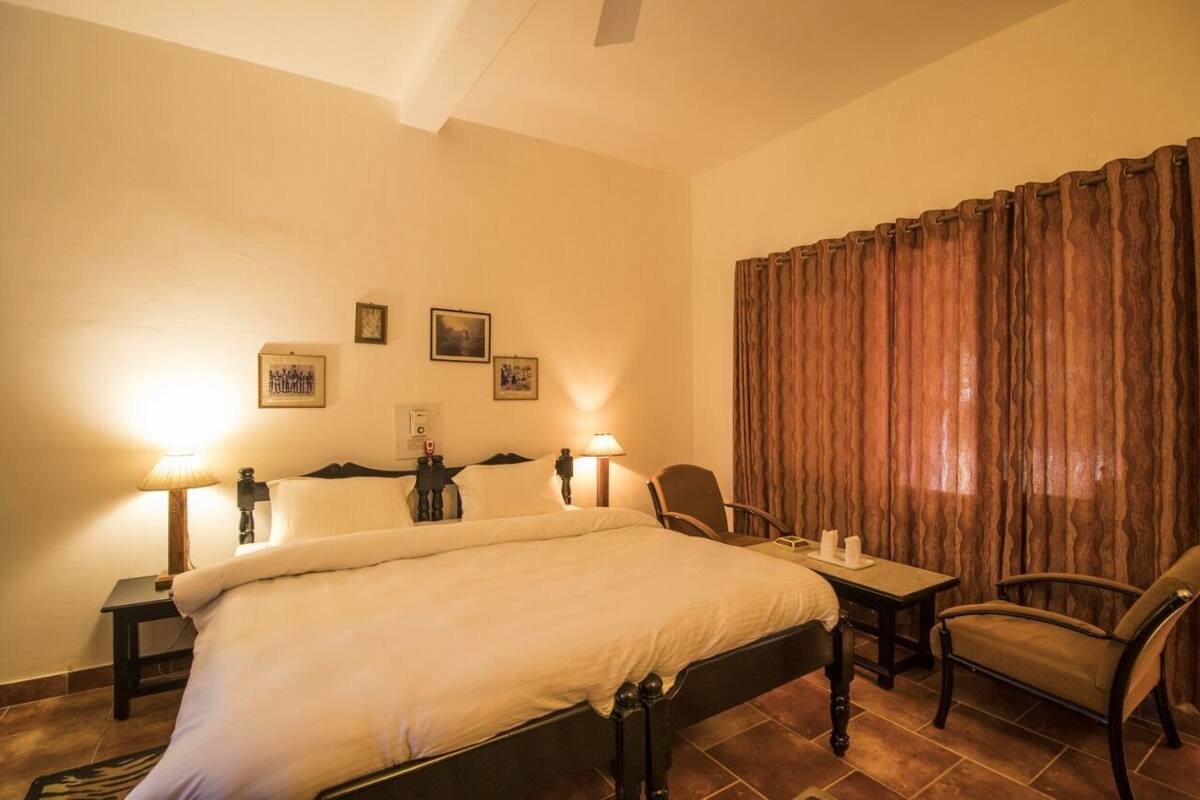 A hotel room with a bed, two bedside lamps, a table with a chair, and a window with curtains.