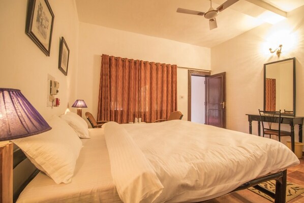 A neatly made bed with a headboard, a desk with a chair, a mirror, and a window with curtains.