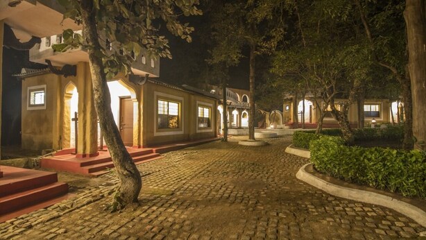 A courtyard with cobblestone paths, a tree, and buildings with illuminated windows at night. - Krishna Jungle Resort  (Bichhiya)