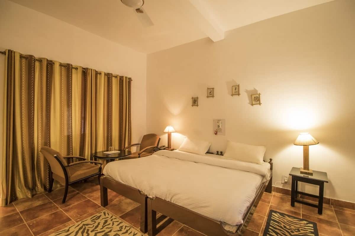 A hotel room with a bed, two chairs, a small table, a nightstand, and a lamp.