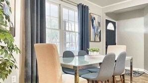 A dining area with a glass table, four chairs, a potted plant, and a window with curtains. - Corporate Stay: 5BR, Guest Suite & Fast WiFi (Decatur)