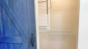 A room with a blue door, a white wall, a window with blinds, and a metal shelf. - Corporate Stay: 5BR, Guest Suite & Fast WiFi (Decatur)