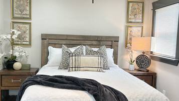 A bedroom with a bed, a ceiling fan, bedside tables, and framed artwork on the walls.