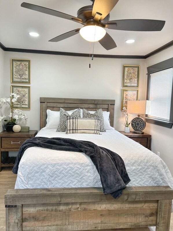 Une chambre à coucher comprenant un lit, un ventilateur de plafond, des tables de chevet et des œuvres d’art encadrées accrochées aux murs.