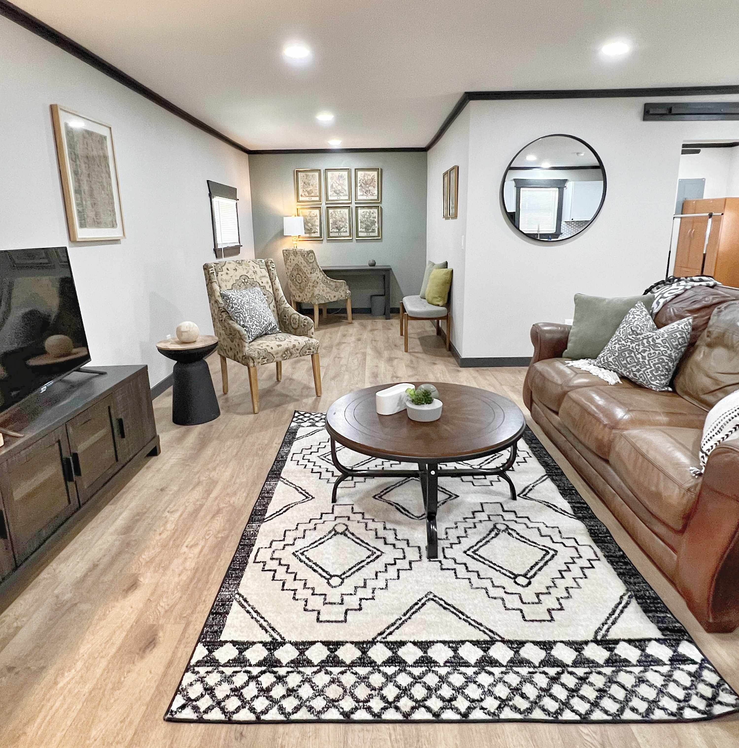 Uma sala de estar com sofá, poltronas, mesa de centro, televisão e tapete.