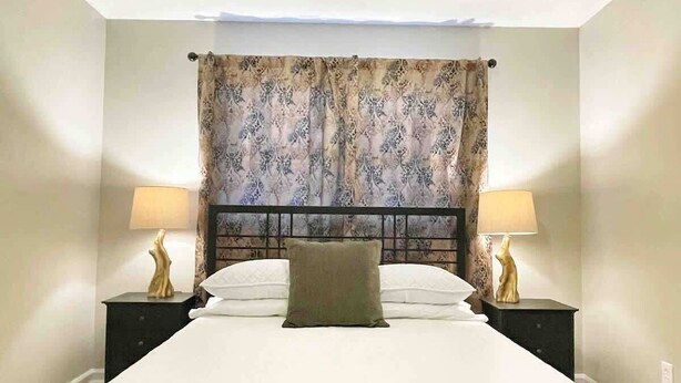A bedroom with a bed, two bedside tables with lamps, a headboard, and a window with curtains. - Corporate Stay: 5BR, Guest Suite & Fast WiFi (Decatur)
