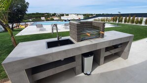 An outdoor kitchen with a sink, a grill, and a pool in the background. - Sky Villa by Laranjal Rentals (Albufeira)