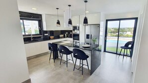 A modern kitchen with a central island, bar stools, and pendant lighting. - Sky Villa by Laranjal Rentals (Albufeira)