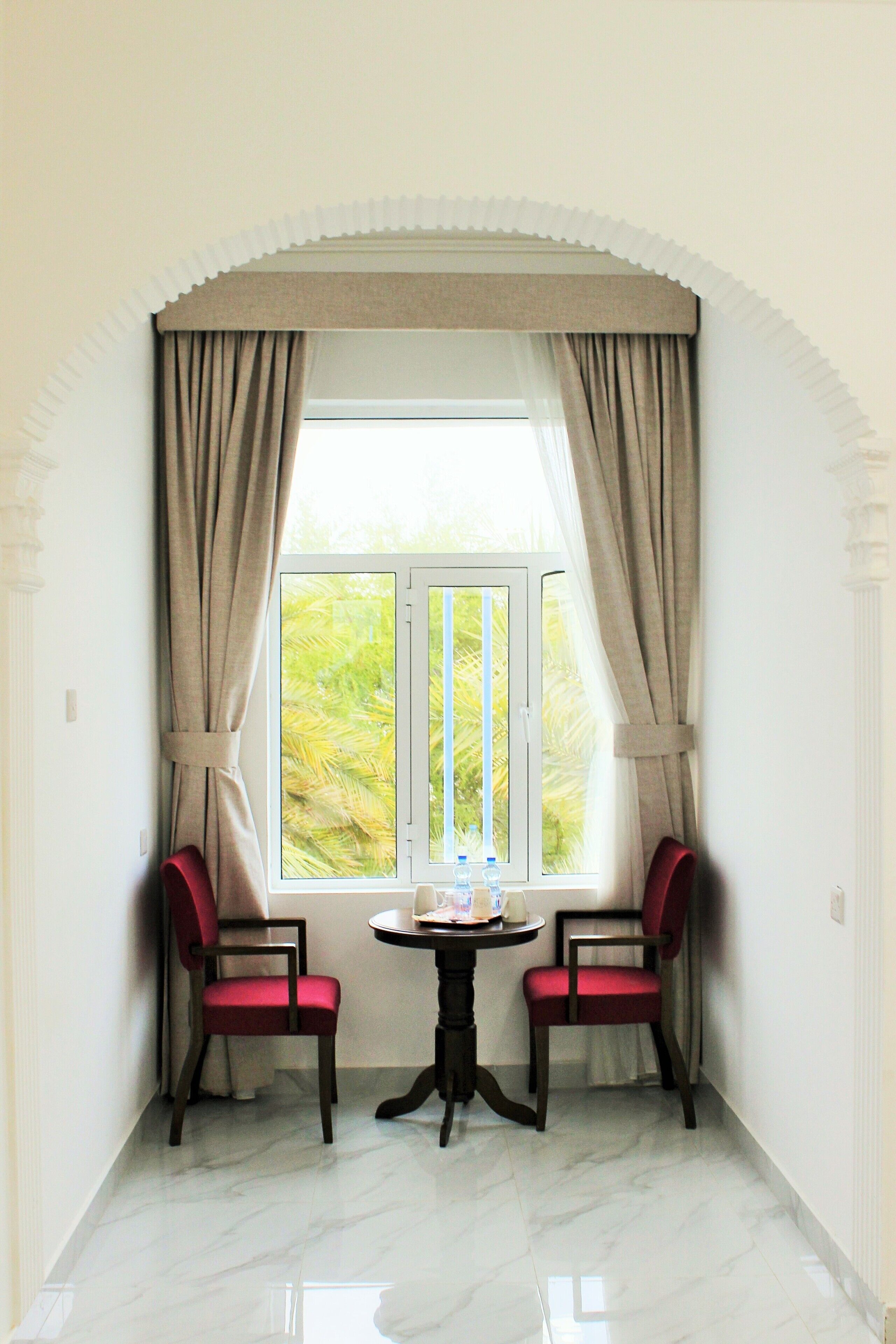A corner room with two red chairs, a small table, and a window with curtains.