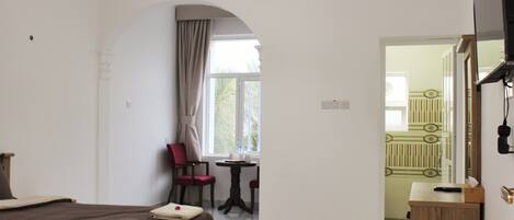 A hotel room with a bed, a small table, a chair, and a view of a balcony.