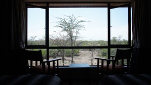 Habitación con un ventanal grande que da a un paisaje natural. Se ven dos sillas de madera y una mesita en primer plano.