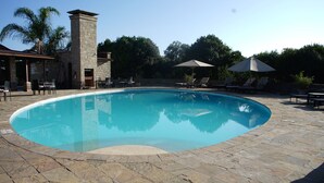 Una piscina con baldosas de piedra, sillas de descanso y sombrillas.