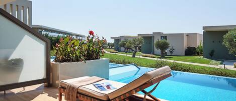 A modern outdoor pool area with a lounge chair and a magazine, surrounded by a well-maintained garden and a clear view of the sky.