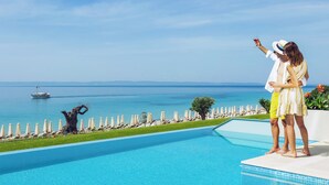 A couple standing by a pool with a view of the sea and a yacht in the distance. - Ammoa Luxury Hotel & Spa Resort (Sithonia)