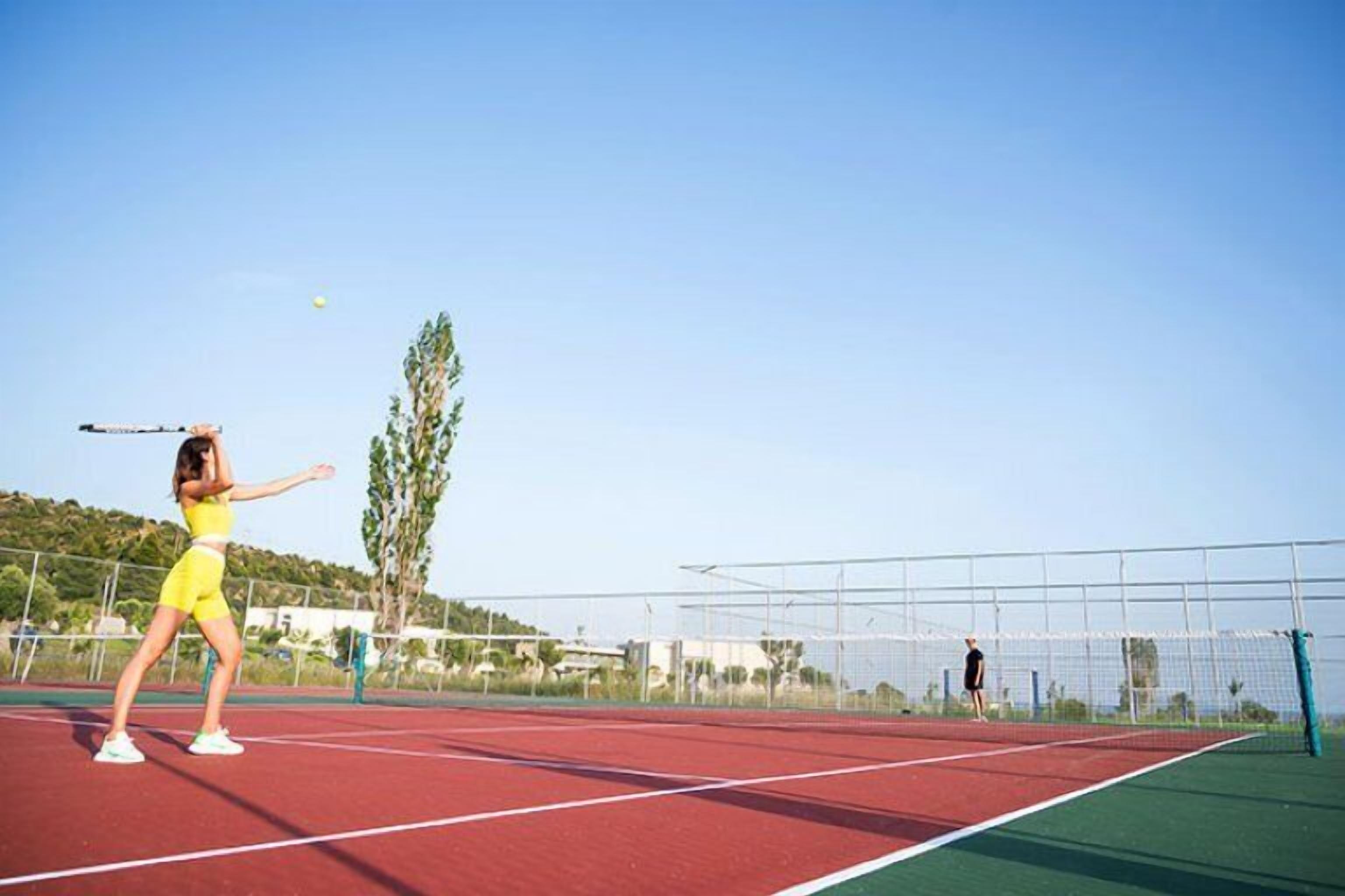 A tennis court with a net, a player in yellow, and another person in the background.