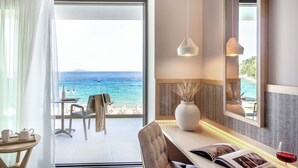A hotel room with a balcony overlooking the sea, a dining table, a chair, and a large mirror. - Ammoa Luxury Hotel & Spa Resort (Sithonia)