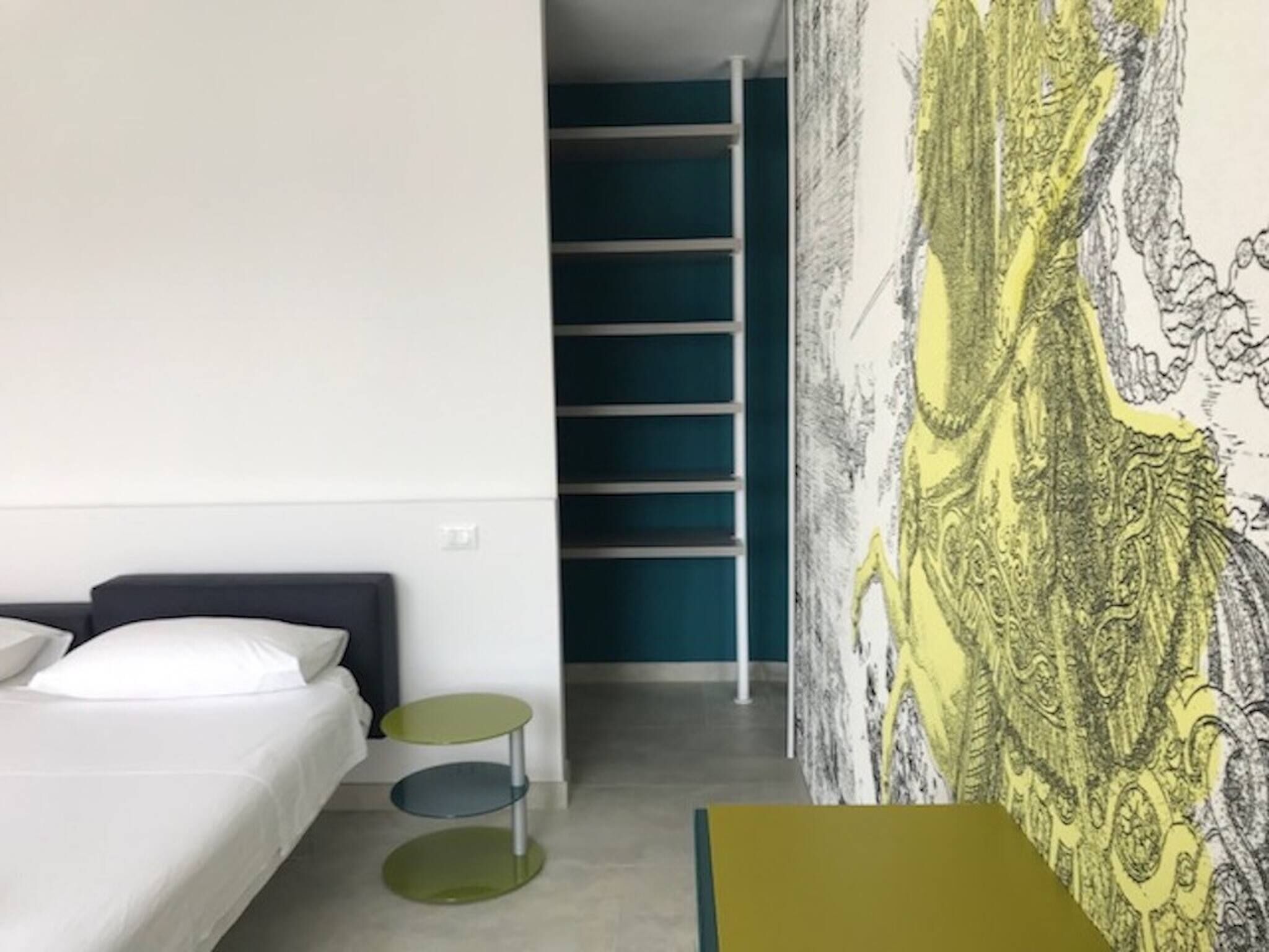 Een moderne hotelkamer met een bed, een klein nachtkastje, een groene fauteuil en een groot abstract schilderij aan de muur.