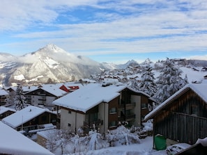A snow-covered mountain village with buildings, including a red house and wooden cabins, and a prominent mountain peak in the background.