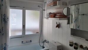 A bathroom with a bathtub, a shower, a toilet, a sink, a mirror, and a window. - Elfe - Apartments Studio Apartment for 2-4 Guests With Amazing View (Emmetten)