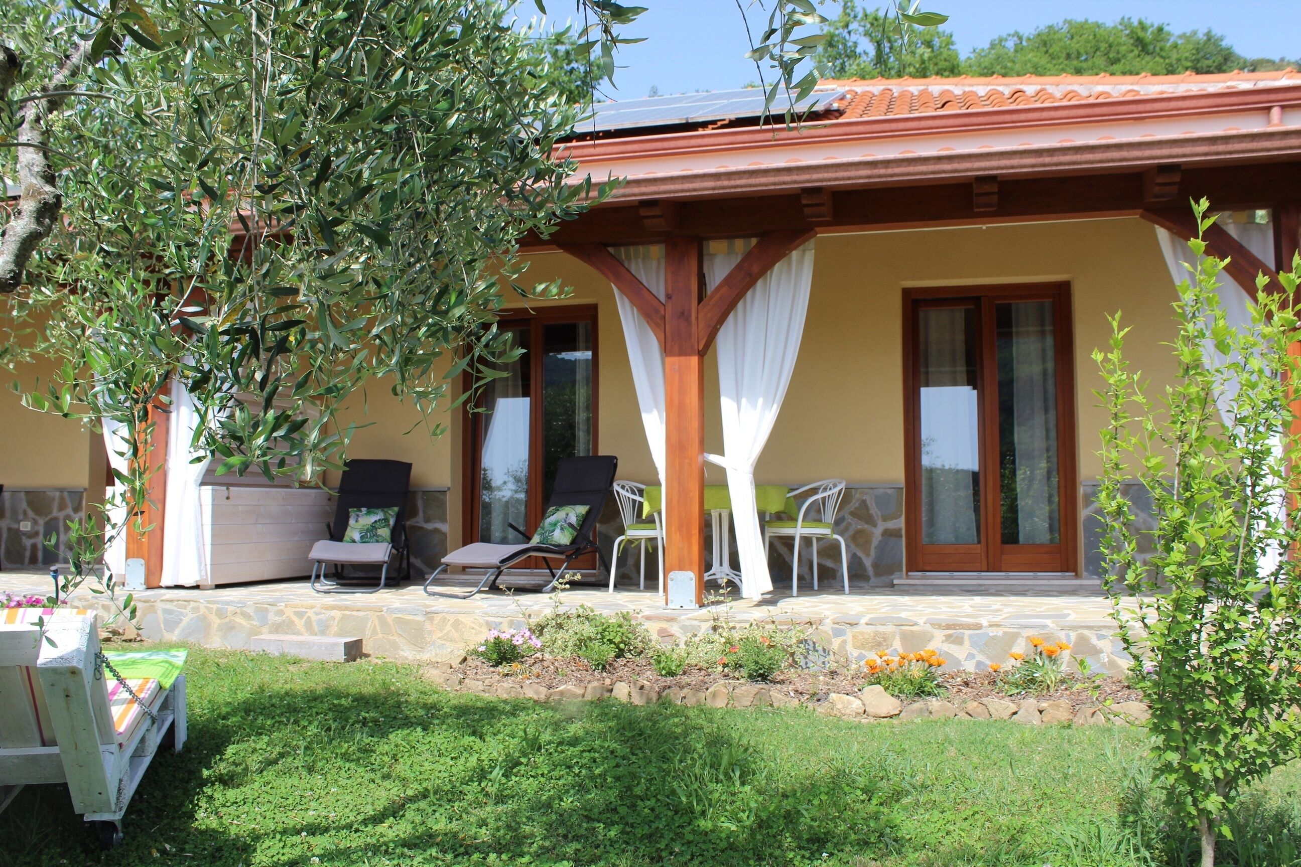 A covered outdoor seating area with a stone floor, surrounded by greenery and a small garden.