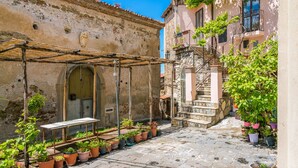 A narrow cobblestone street with a rustic building on one side and a staircase leading to a balcony on the other. There are potted plants and a wooden table under a pergola. - Ecolodge Selvitelle - Sustainable Retreat Amidst Olive Groves in Cilento (Cicerale)